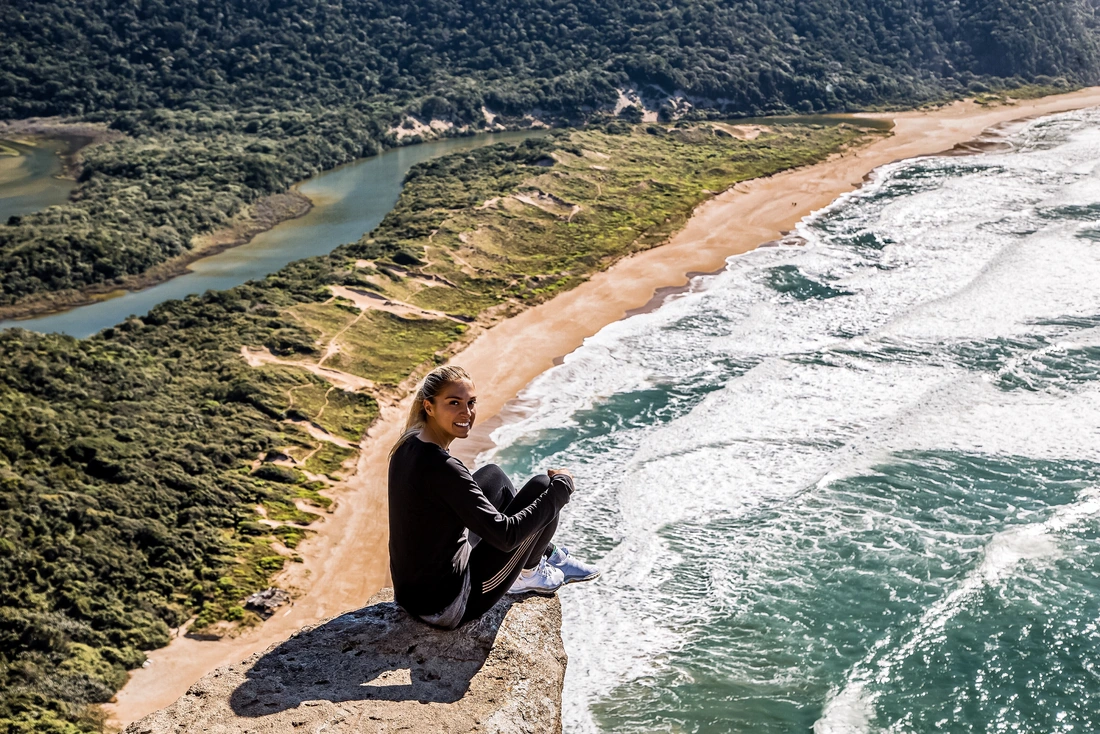 Elena Frosch sitzt auf einem Felsen, im Hintergrund sieht man Meer und Strand