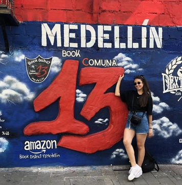 Elona leaning against a wall on which is written Medellín