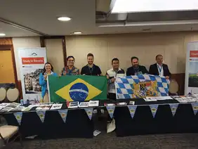 Foto von Felix Reinhardt mit fünf brasilianischen Kolleginnen und Kollegen, die die Bayerische und die Brasilianische Fahne halten.