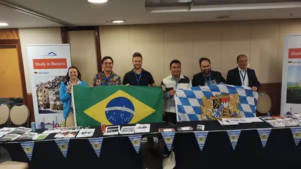 Foto von Felix Reinhardt mit fünf brasilianischen Kolleginnen und Kollegen, die die Bayerische und die Brasilianische Fahne halten.